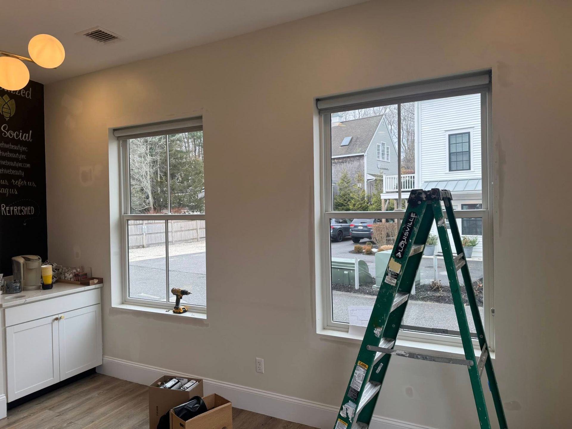 Partially renovated room with two windows, a green ladder, and a white cabinet under the left window.