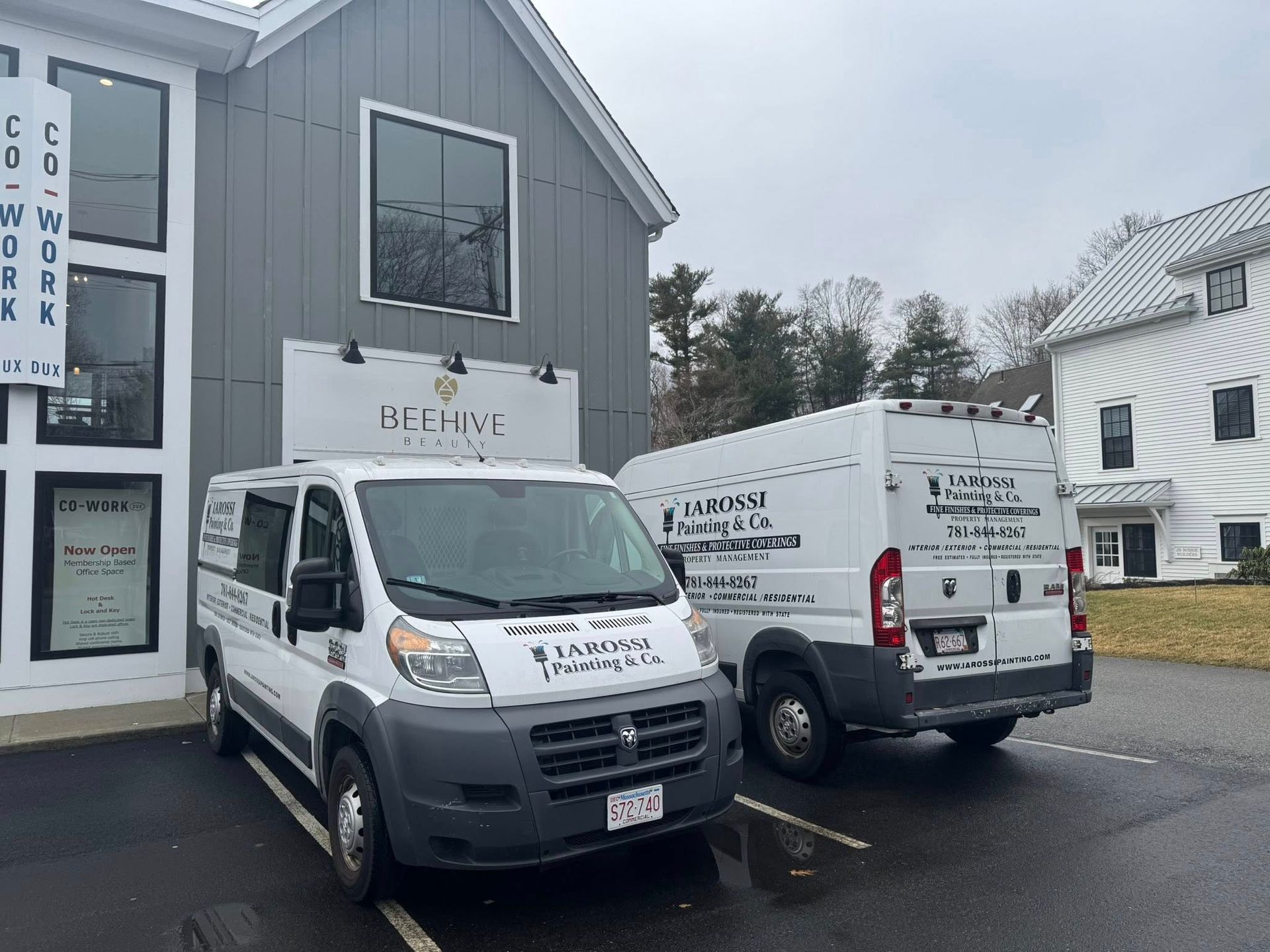 Two white service vans parked outside a gray building on a wet lot