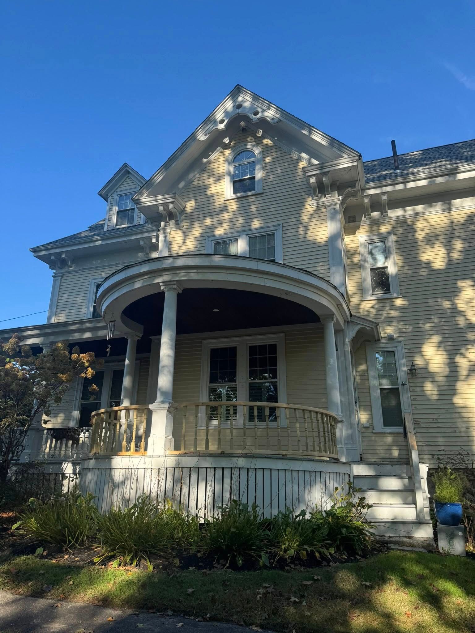 Victorian-style house with a wraparound porch and sunlit siding under a blue sky