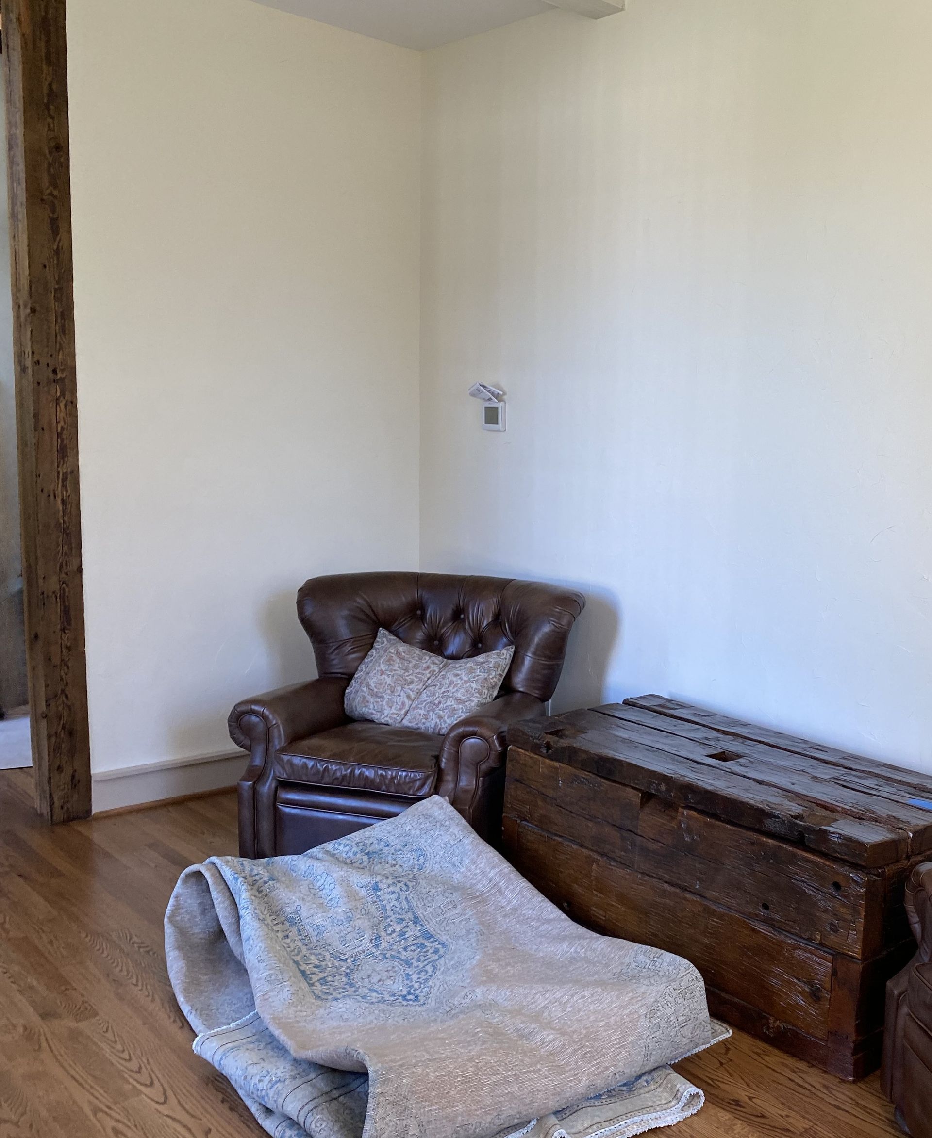 A living room with a chair , trunk and rug on the floor.