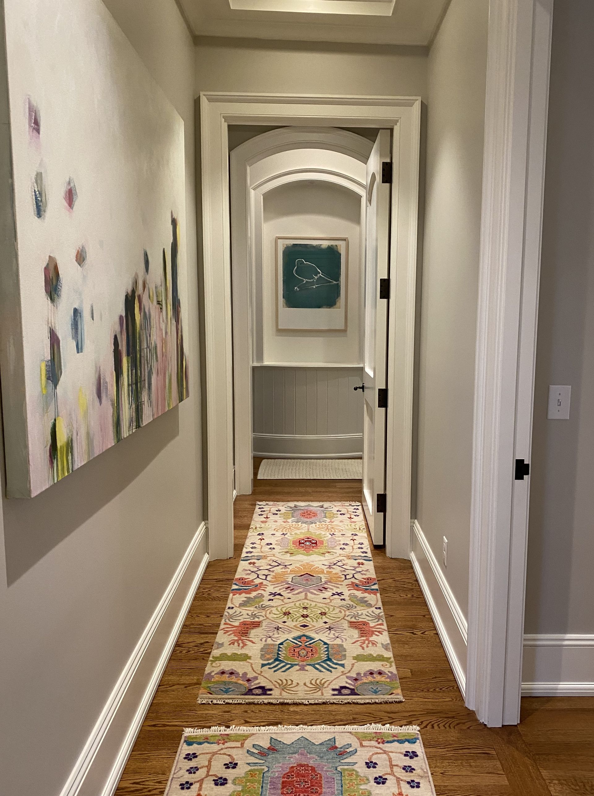 A long hallway with a rug and paintings on the wall.