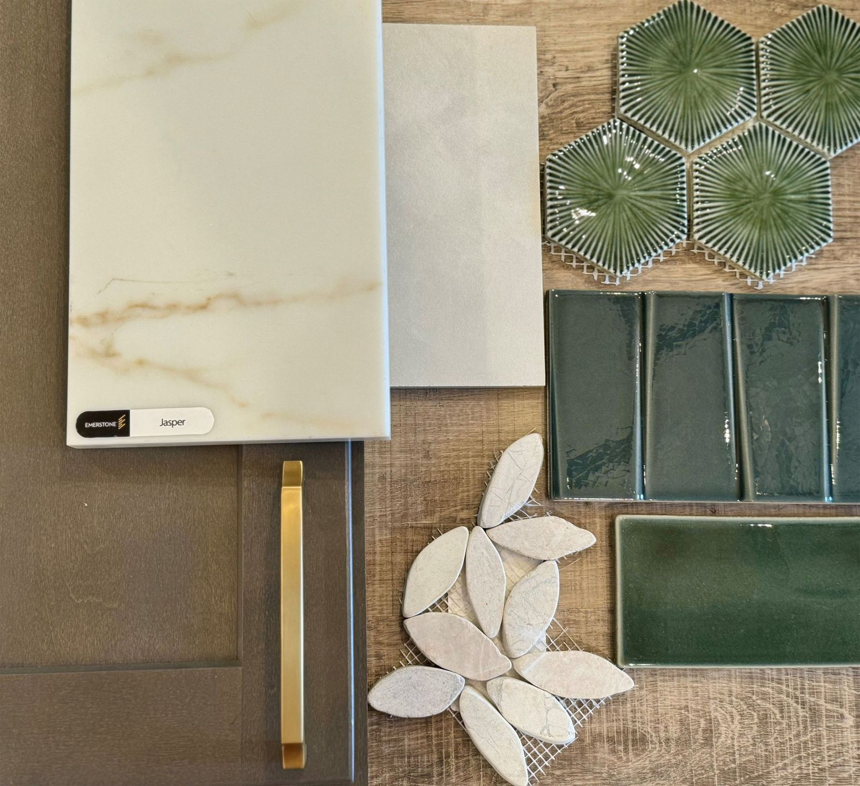 Sample board of various tiles and materials in shades of white, green, and brown, with a gold handle.