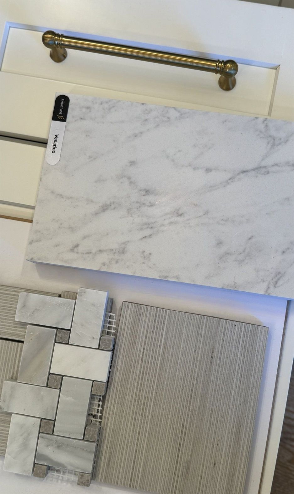 A display of interior design samples: white cabinet door, marble countertop, mosaic tile, textured fabric.