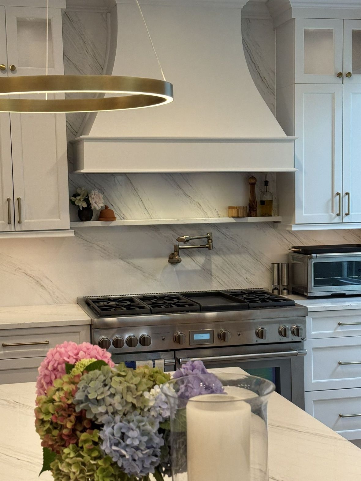 Stylish white kitchen with marble accents, range, and floral arrangement.