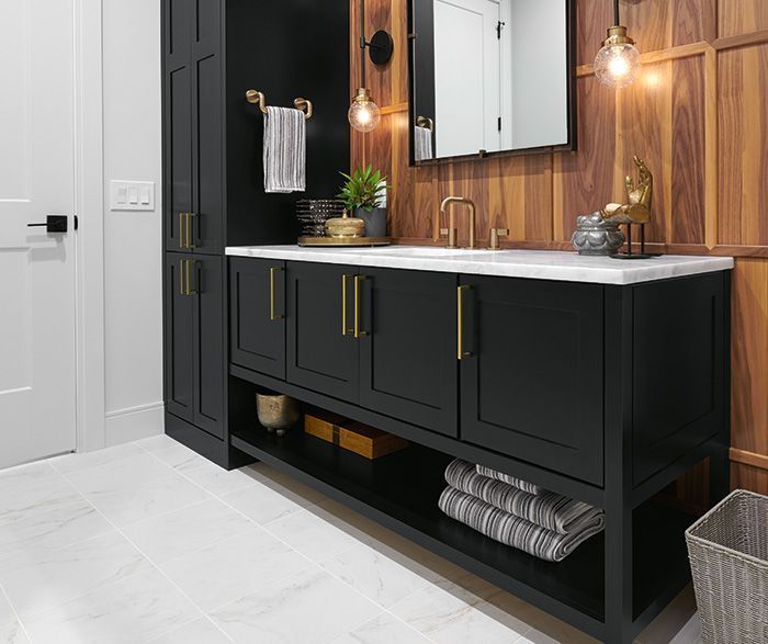 Black vanity with gold hardware in a bathroom with wood paneling and white tile.
