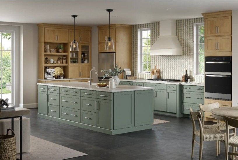 Green kitchen island with light wood cabinets, dark floors, and white backsplash.