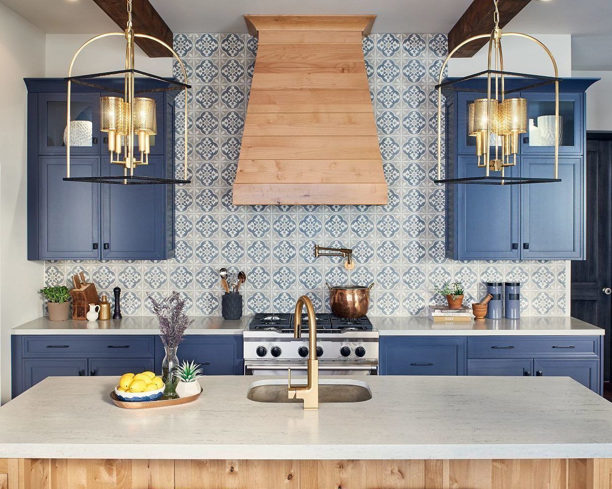 Kitchen with blue cabinets, patterned backsplash, wooden hood, and gold light fixtures.