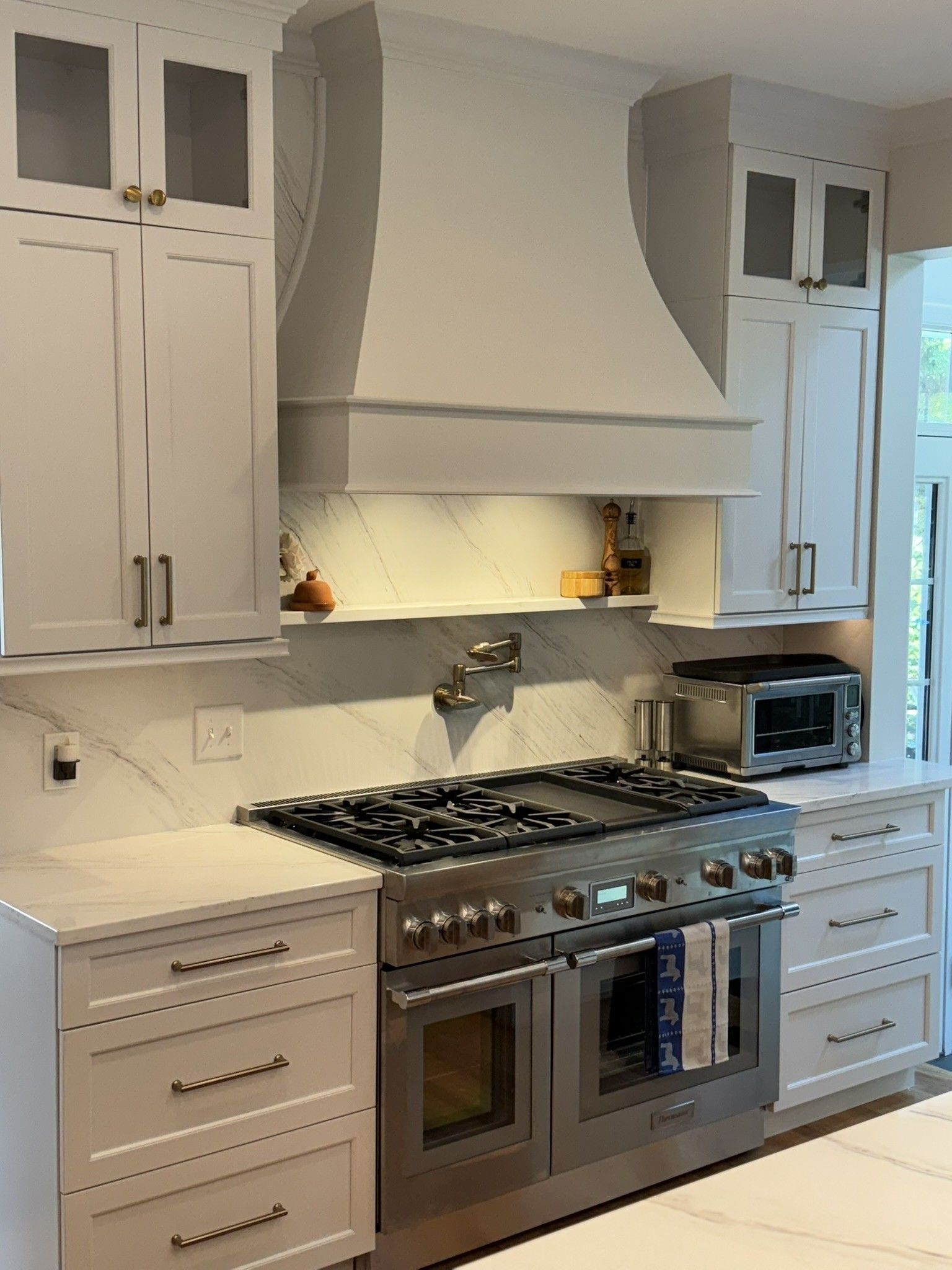White kitchen with stainless steel range, custom hood, and cabinetry.