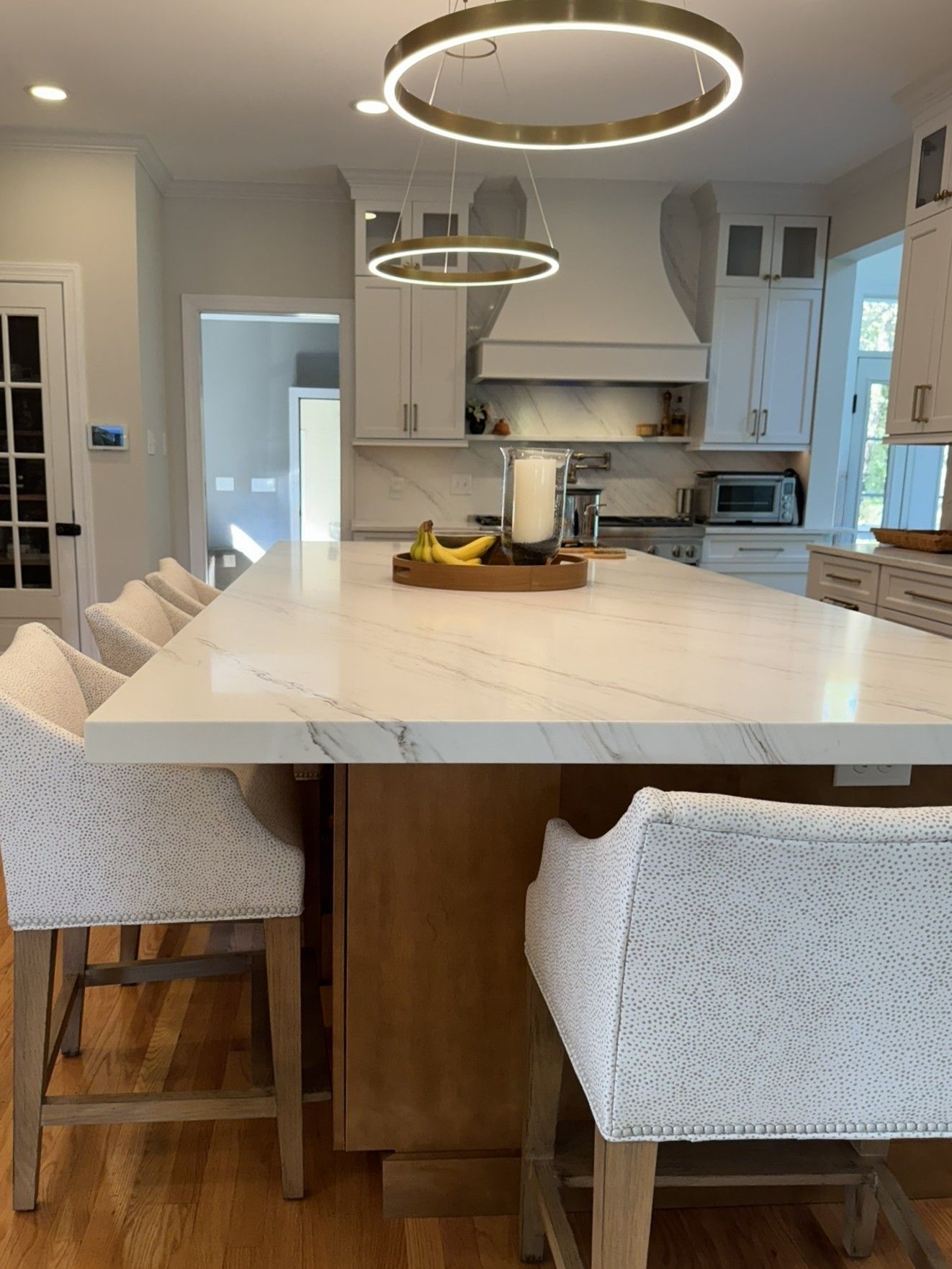 Spacious kitchen with large island, light cabinets, and ring pendant lights. Barstools line the island.
