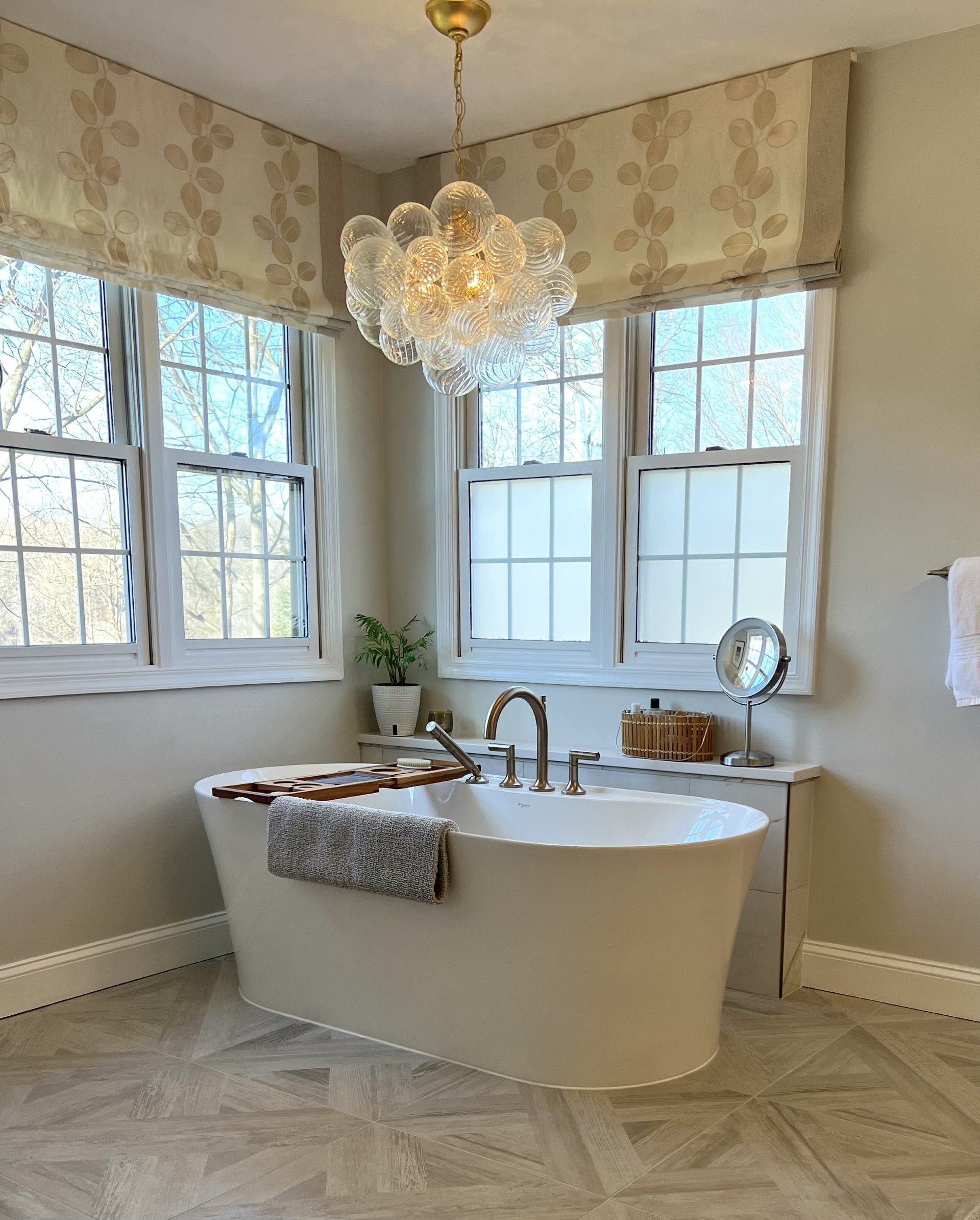 A luxurious bathroom with a freestanding tub beneath a window and a chandelier.
