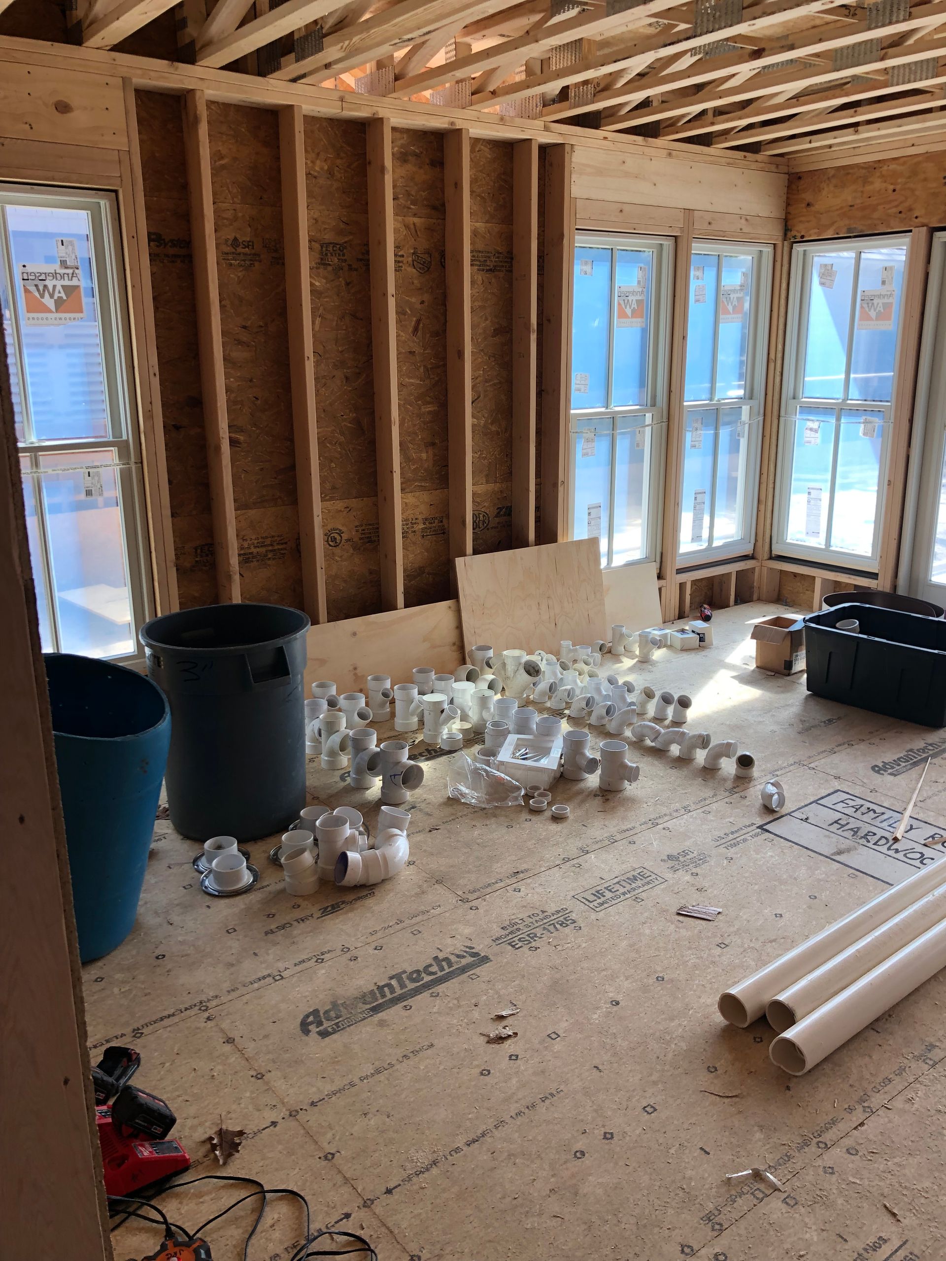 A room under construction with a lot of pipes on the floor.