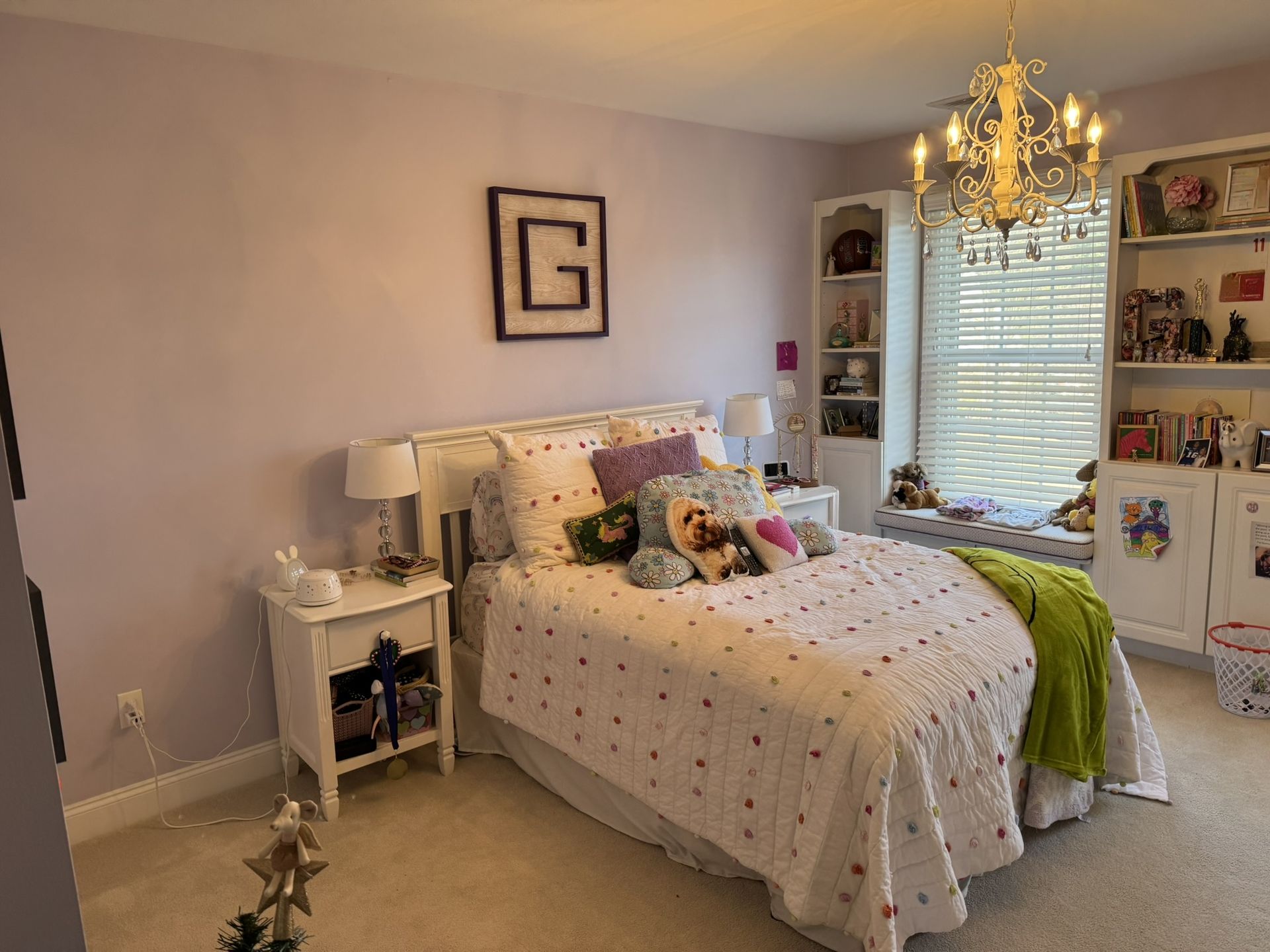 A bedroom with a bed , nightstands , shelves and a chandelier.