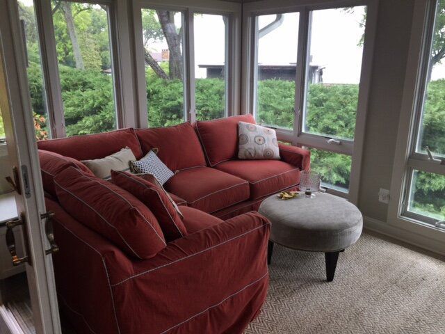 A living room with a red couch, ottoman, and lots of windows.