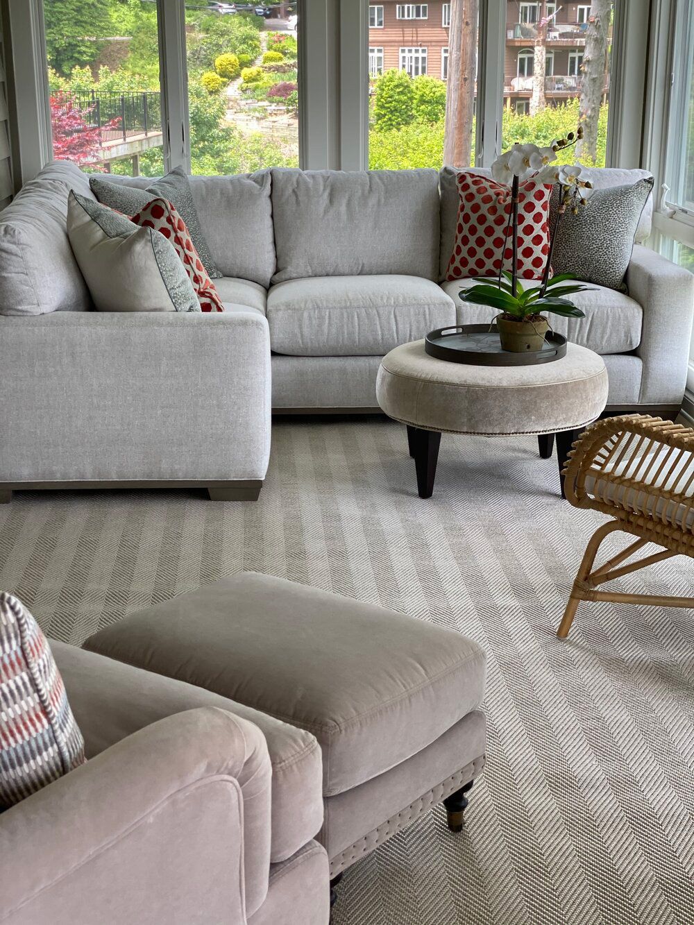 A living room with a sectional couch, chairs, ottoman, and wicker chair.