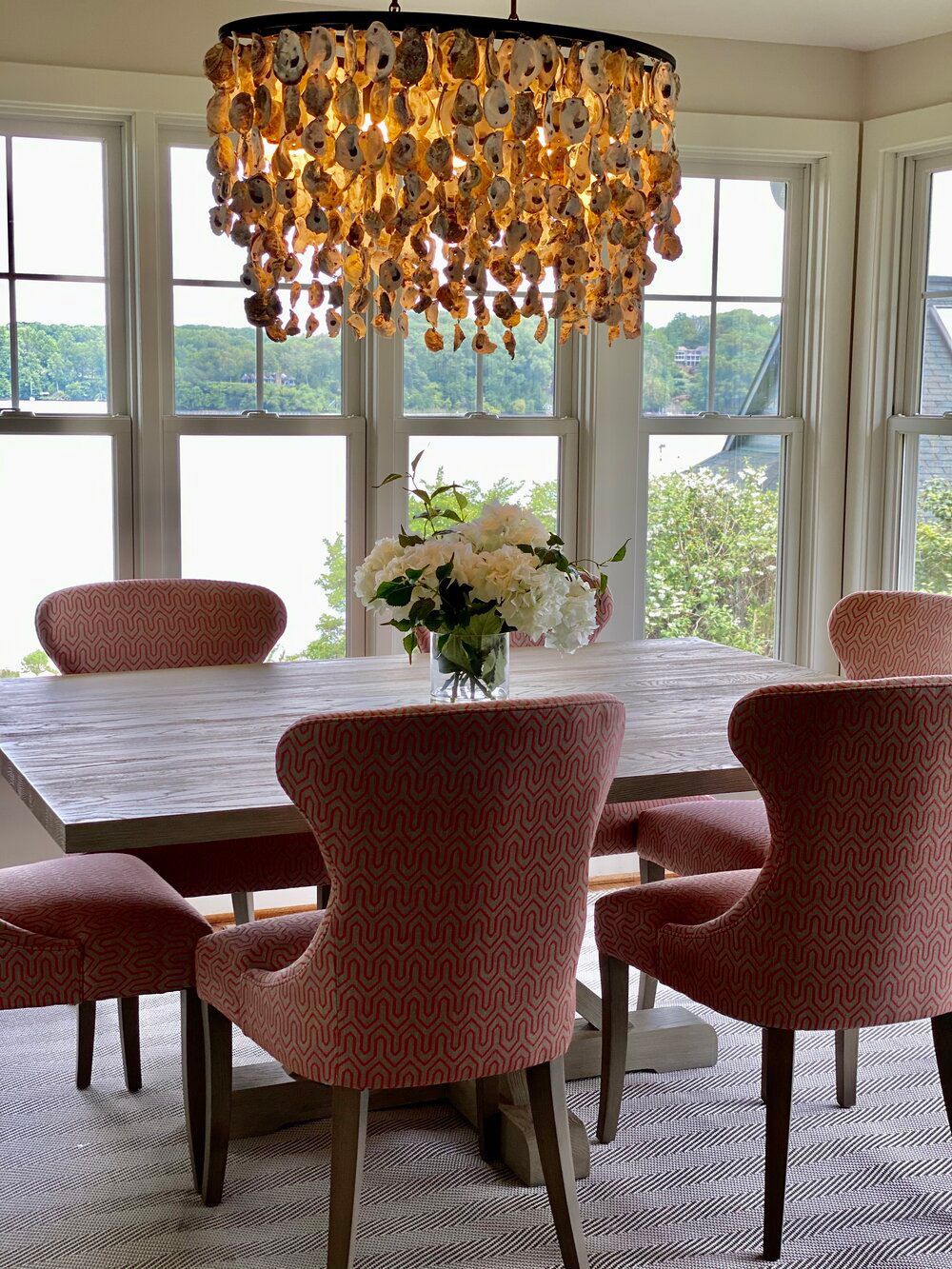 A dining room with a table and chairs and a chandelier made of seashells.