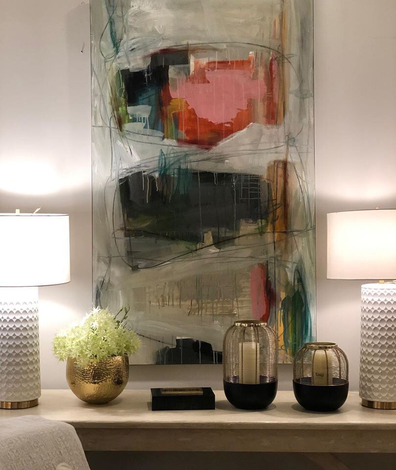 A living room with a large painting on the wall , lamps , vases and candles.