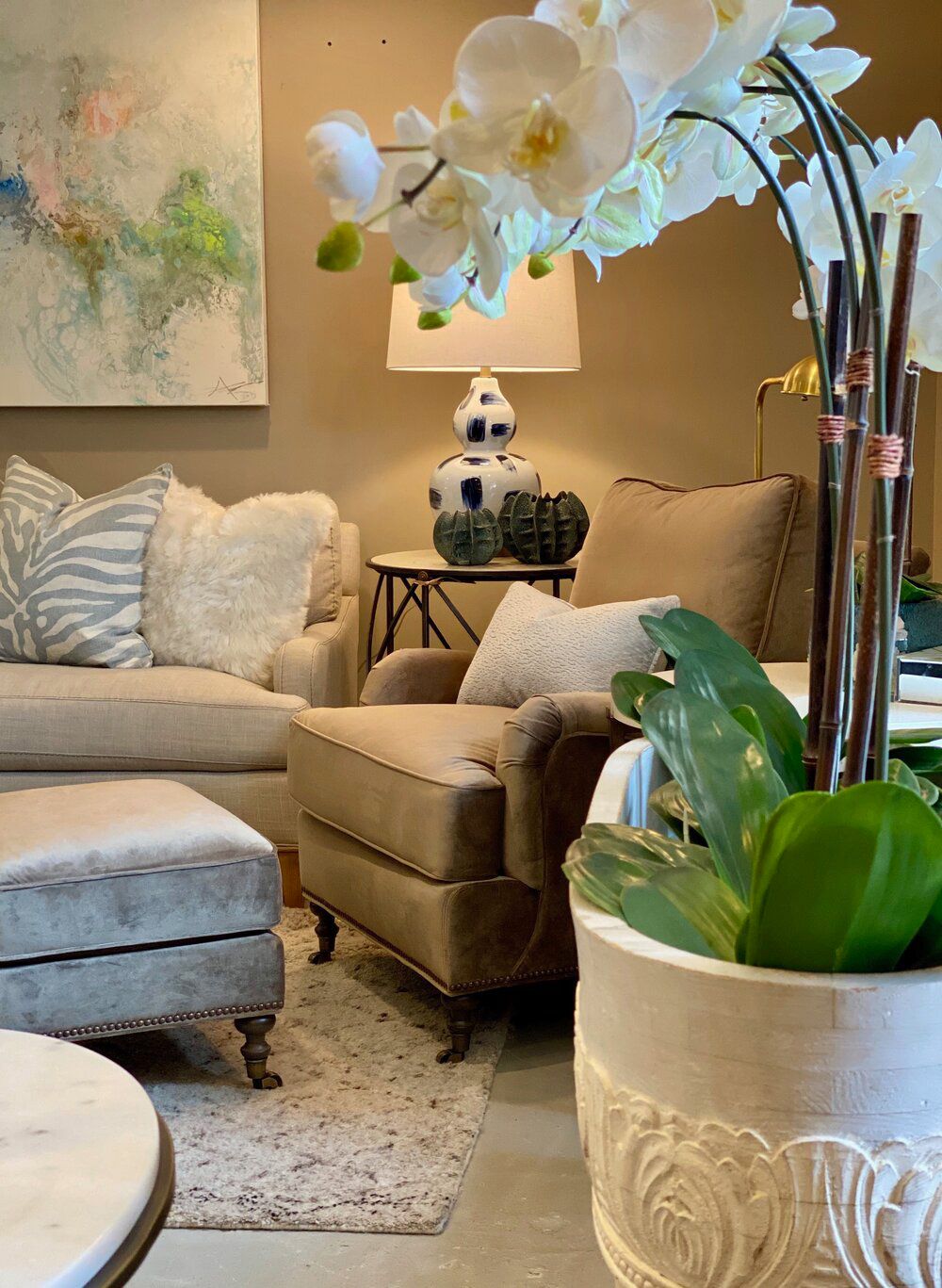 A living room with a couch , chair , ottoman and a potted plant.