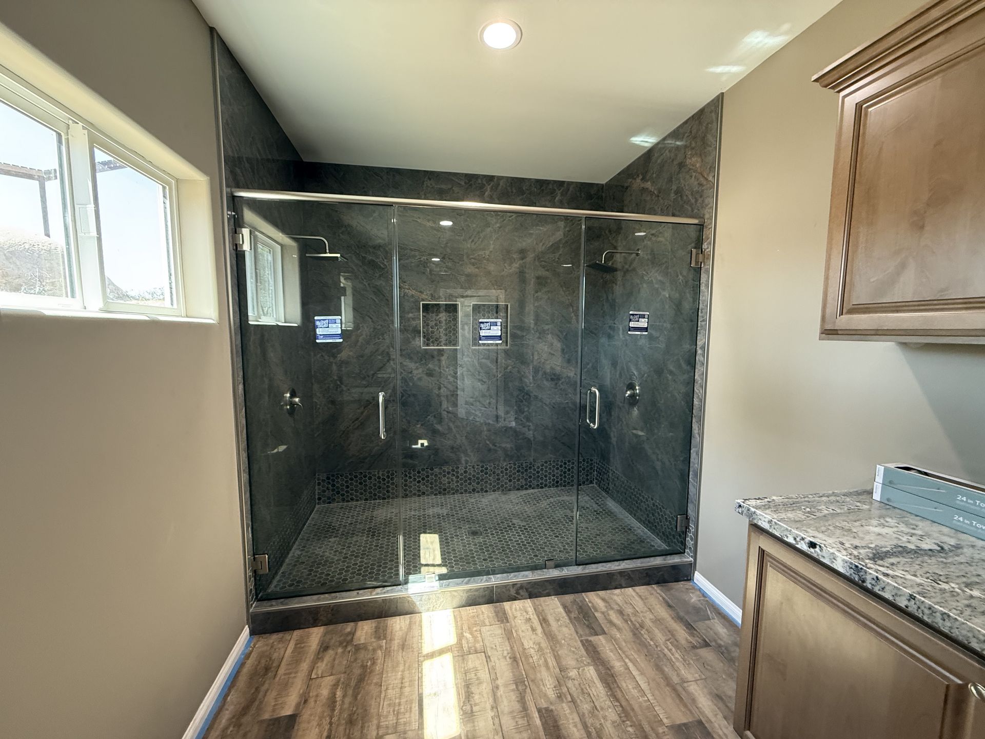 Modern bathroom with dark marble shower, wood-look floor, and granite vanity cabinets