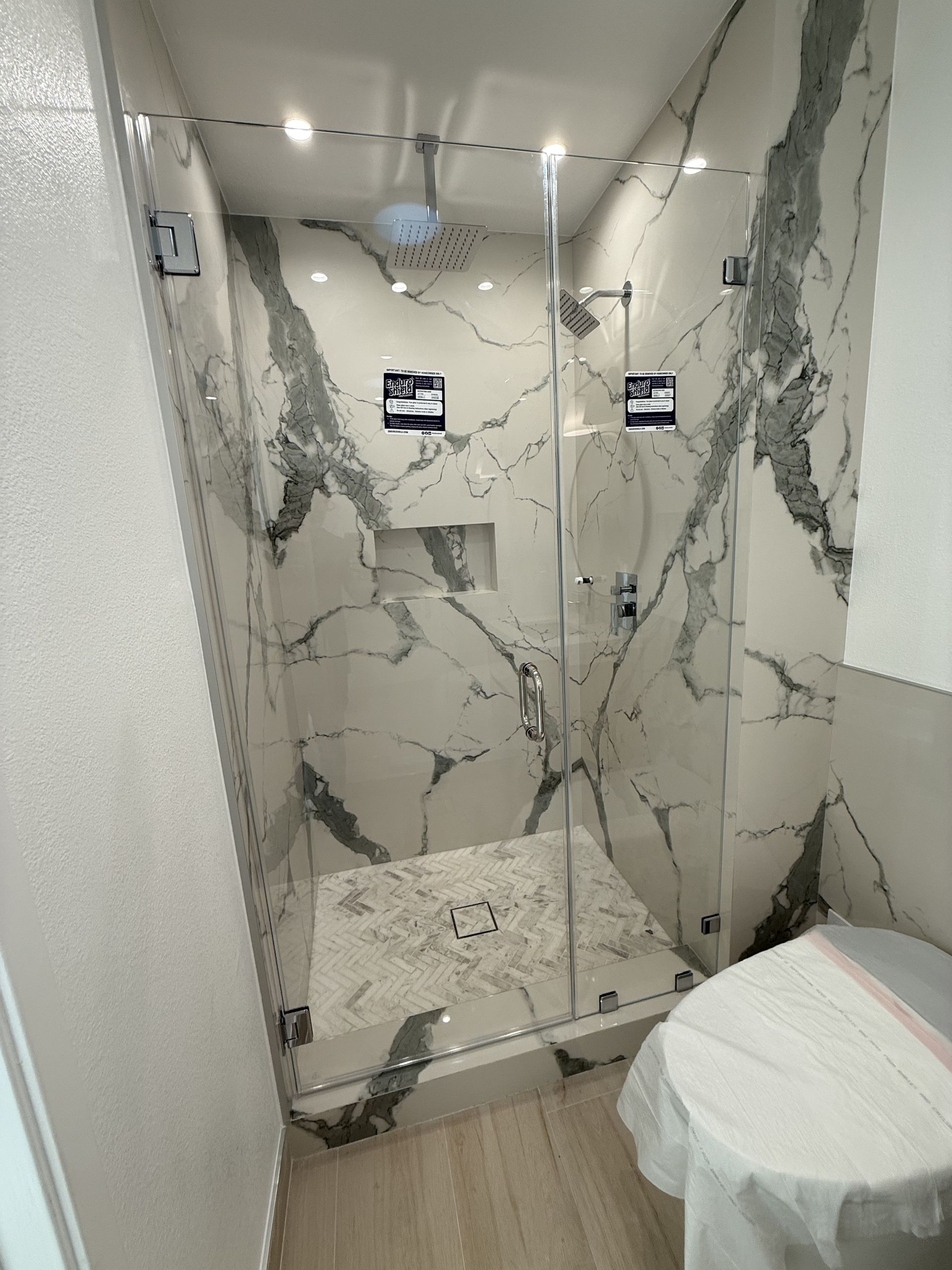 Marble-tiled shower with glass door, ceiling light, and a toilet in the foreground