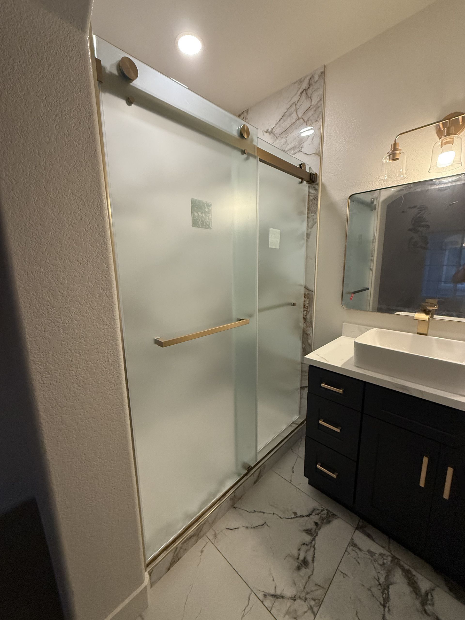 Modern bathroom with frosted glass shower doors, marble tile floor, and vanity sink.