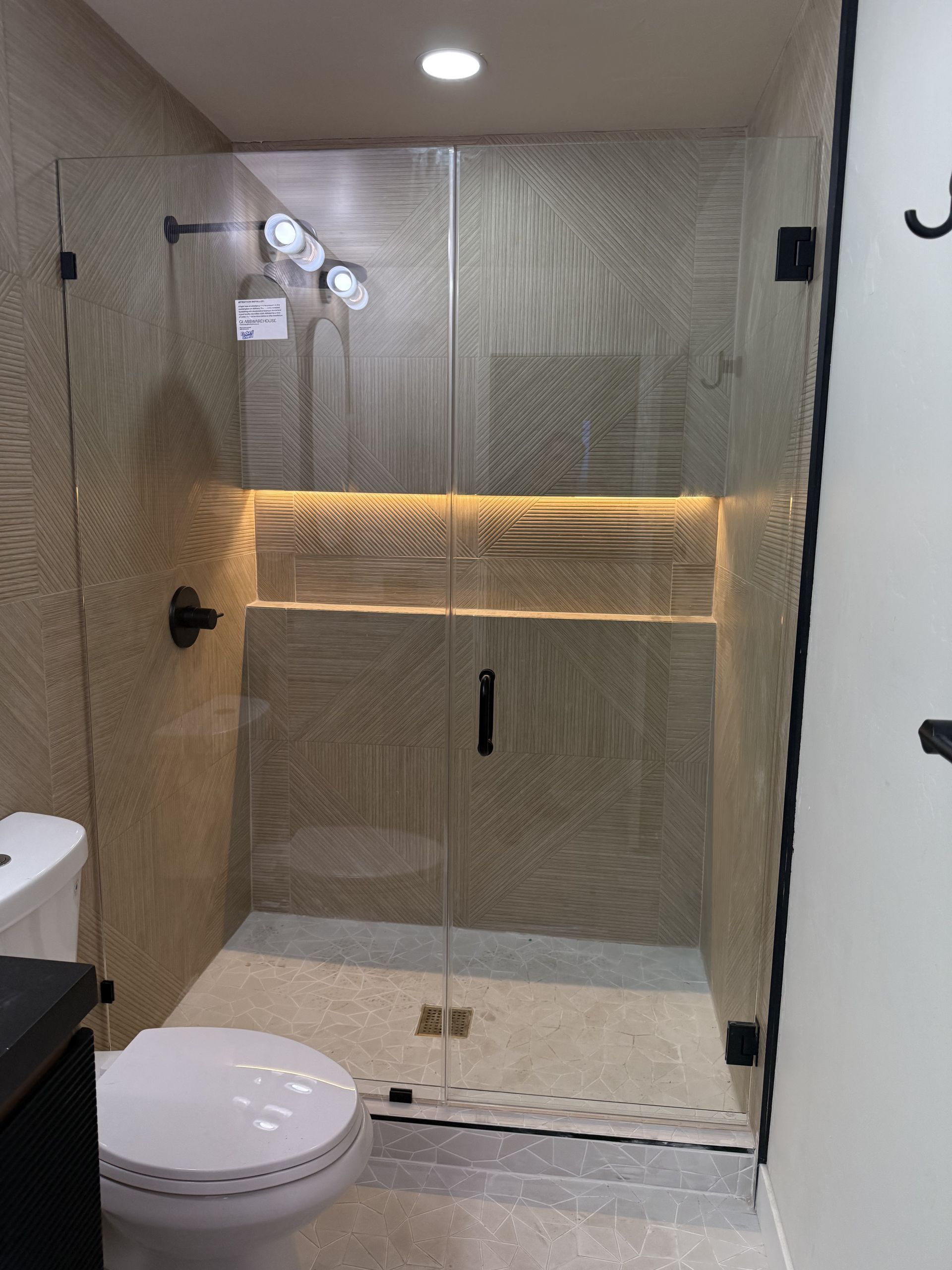 Modern bathroom with glass shower enclosure, toilet, and lit vanity mirror area