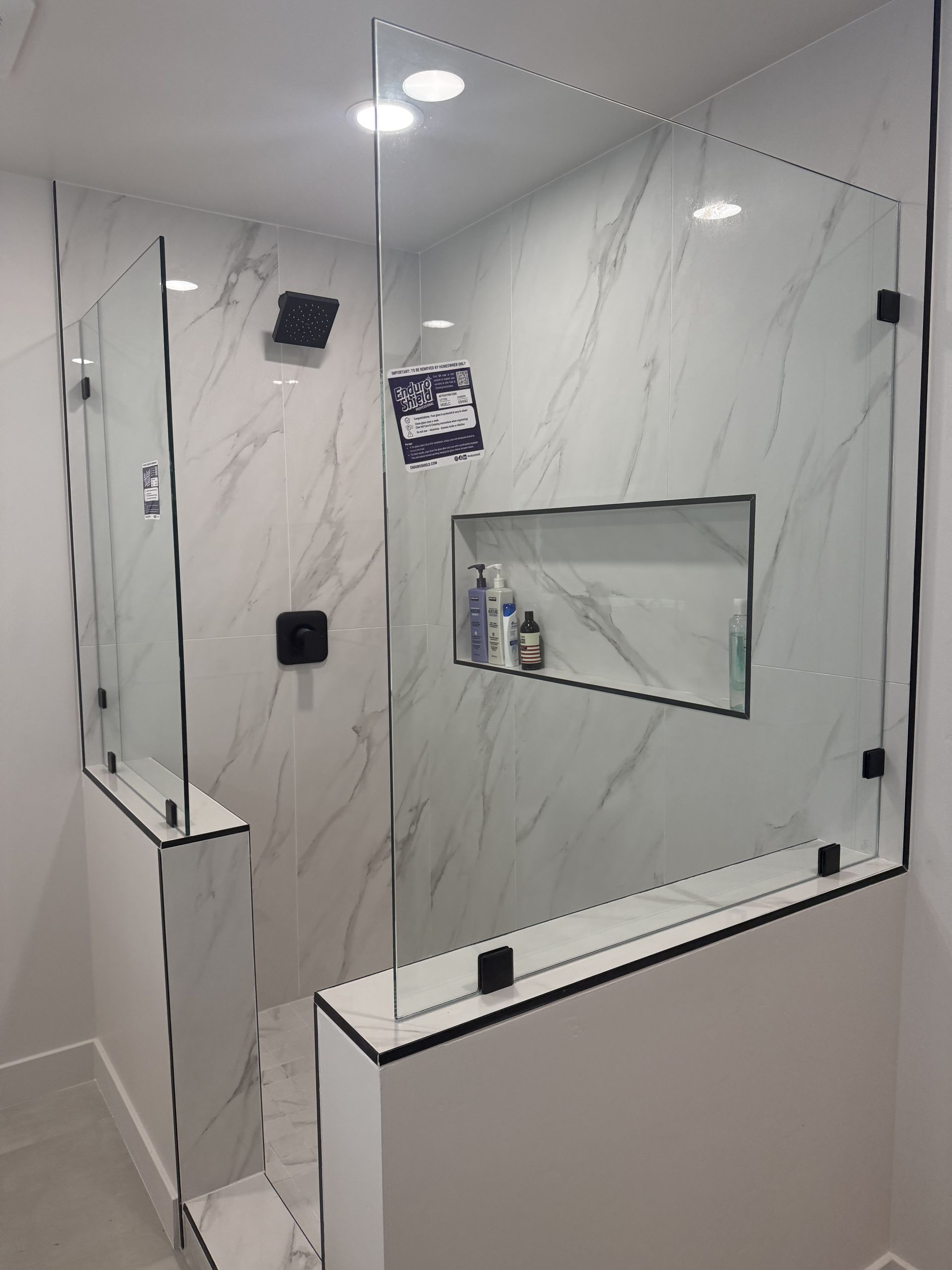 Modern shower with marble-look tiles, glass enclosure, and built-in recessed shelf.