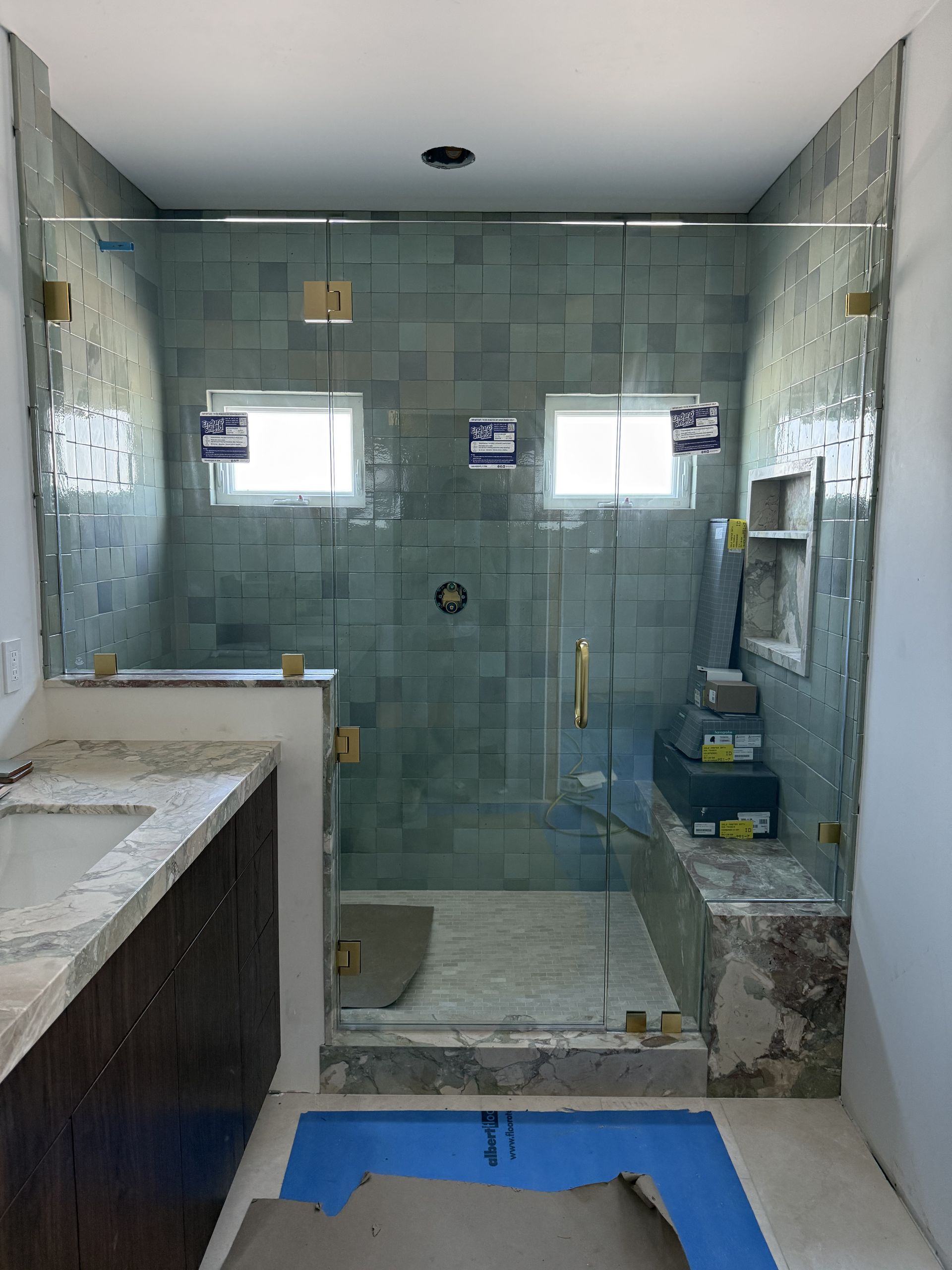 Unfinished bathroom with glass shower enclosure, tiled walls, sink counter, and blue floor covering.