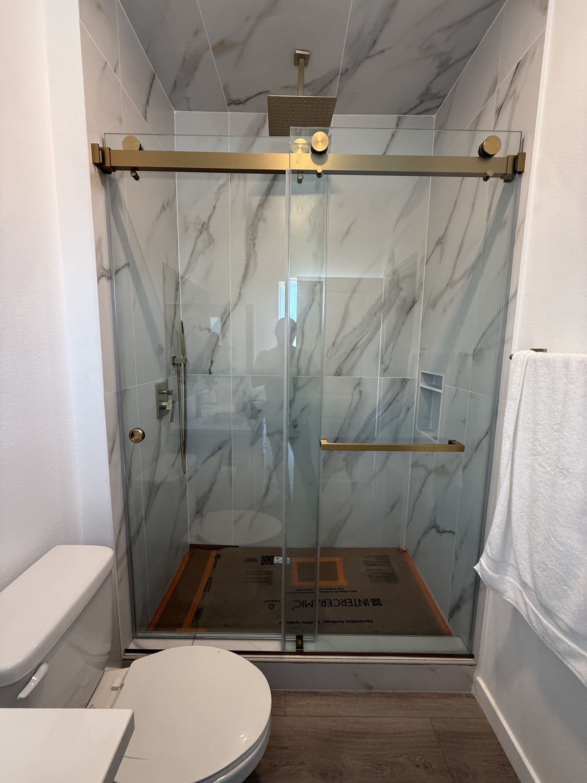 Bathroom with glass shower enclosure, marble-look walls, and a toilet in the foreground
