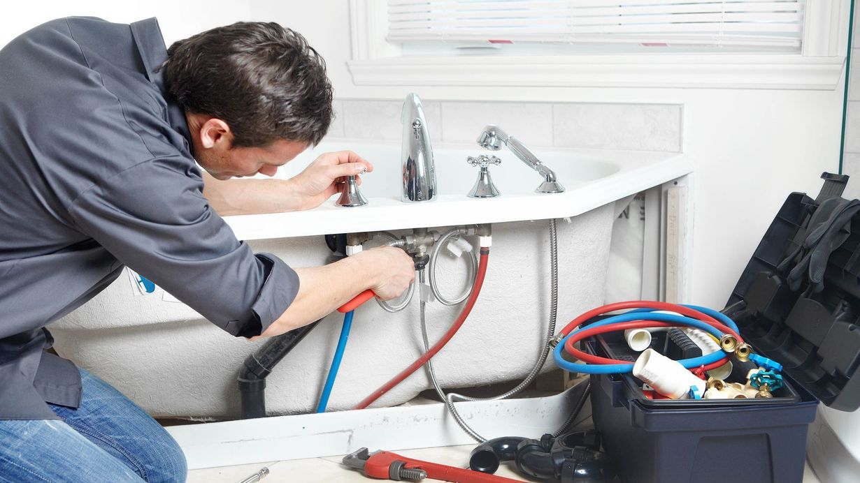 Plumber inspecting pipes under a sink with tools and hoses in a bathroom cabinet