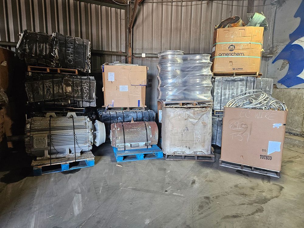 Assorted metal materials on pallets inside a warehouse. Boxes and industrial objects stacked.