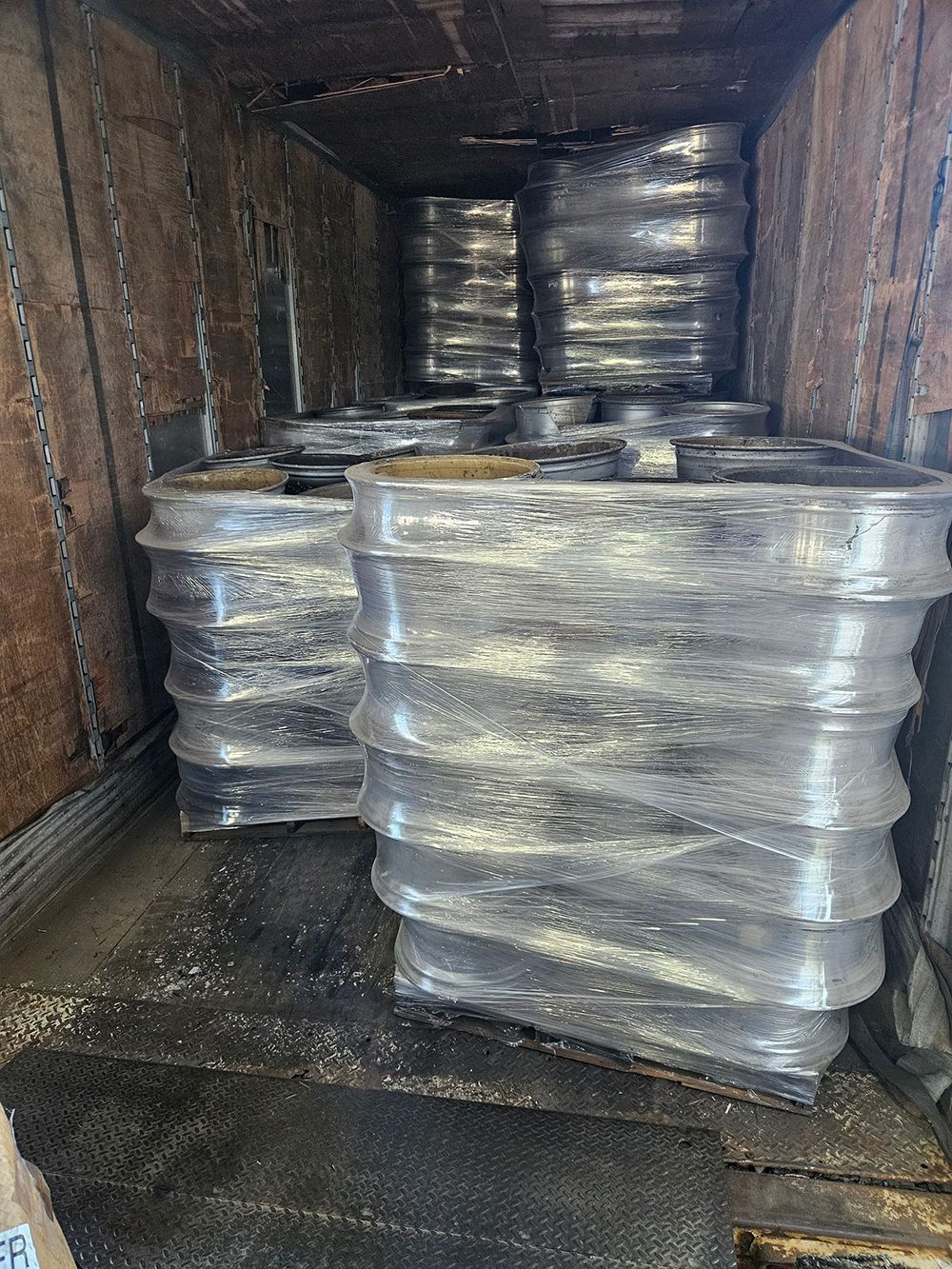 Large, cylindrical metal objects wrapped in plastic, stacked inside a truck.