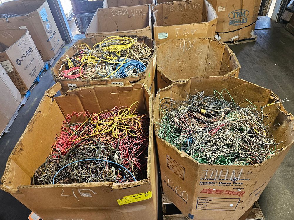 Cardboard boxes filled with colorful electrical wires, likely scrap, in an industrial setting.