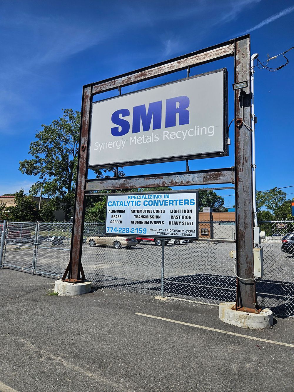 Sign for SMR Scrap Metals Recycling. Steel frame, blue sky, sign with business details below.