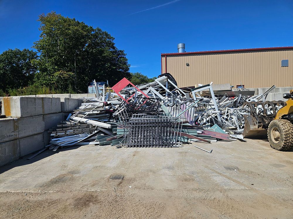 Pile of scrap metal at a recycling facility, with a building and sky in the background.