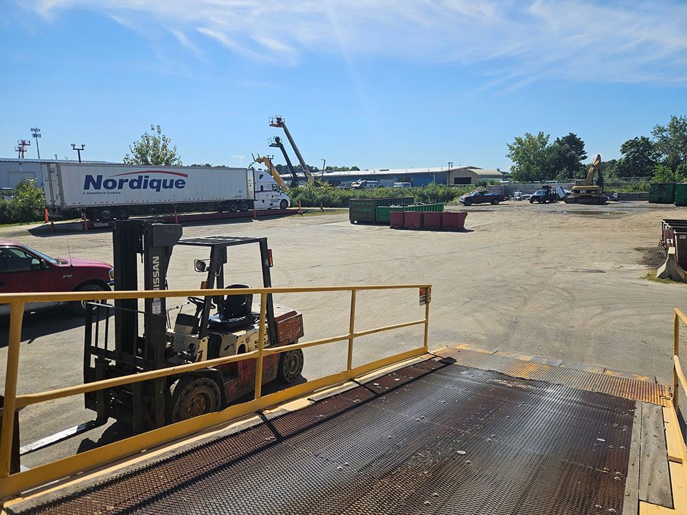 Forklift in a recycling yard with a Nordique truck and machinery on a sunny day.
