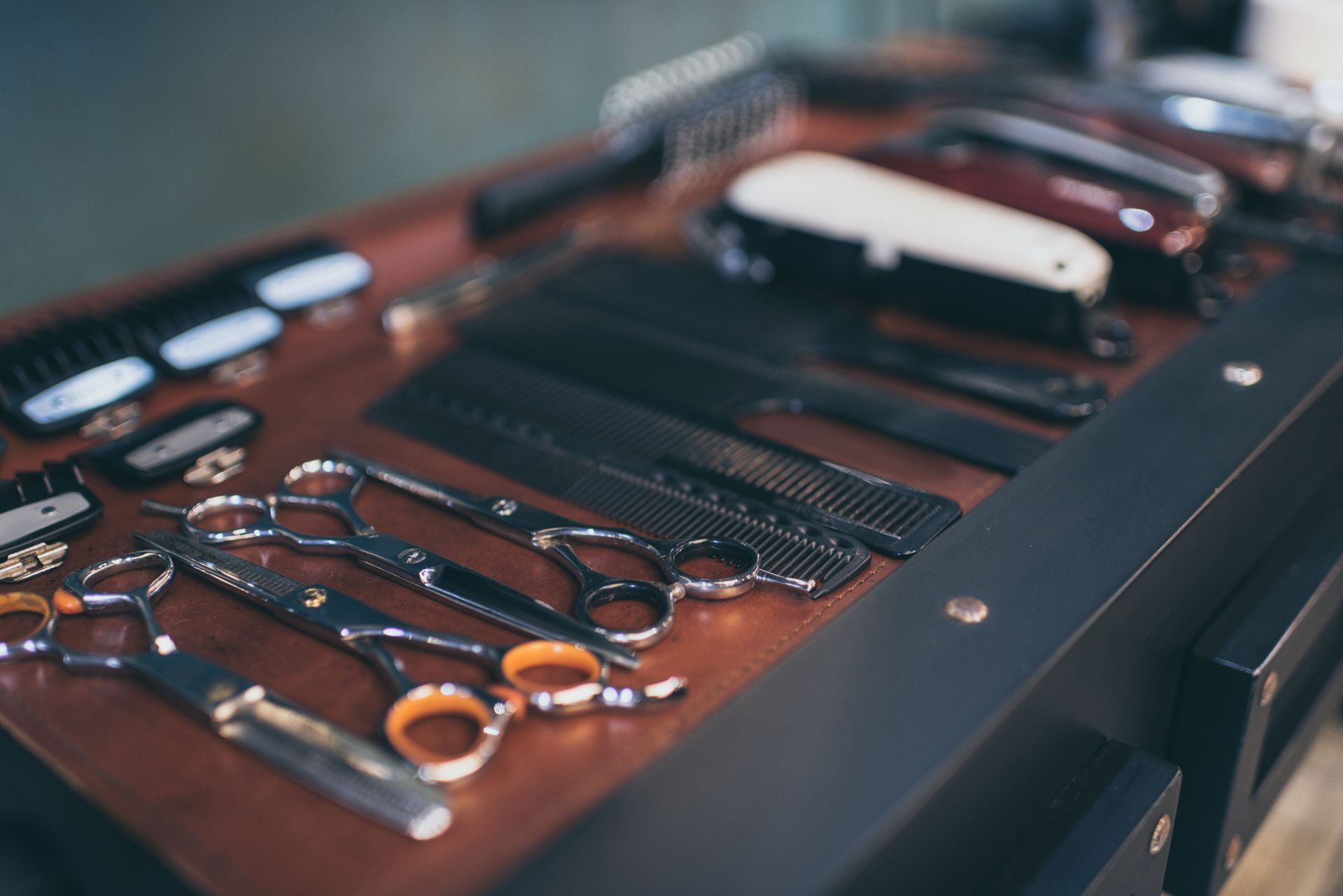 Barber tools, including metal shears, various combs, and electric clippers, are arranged neatly on a dark wooden surface.