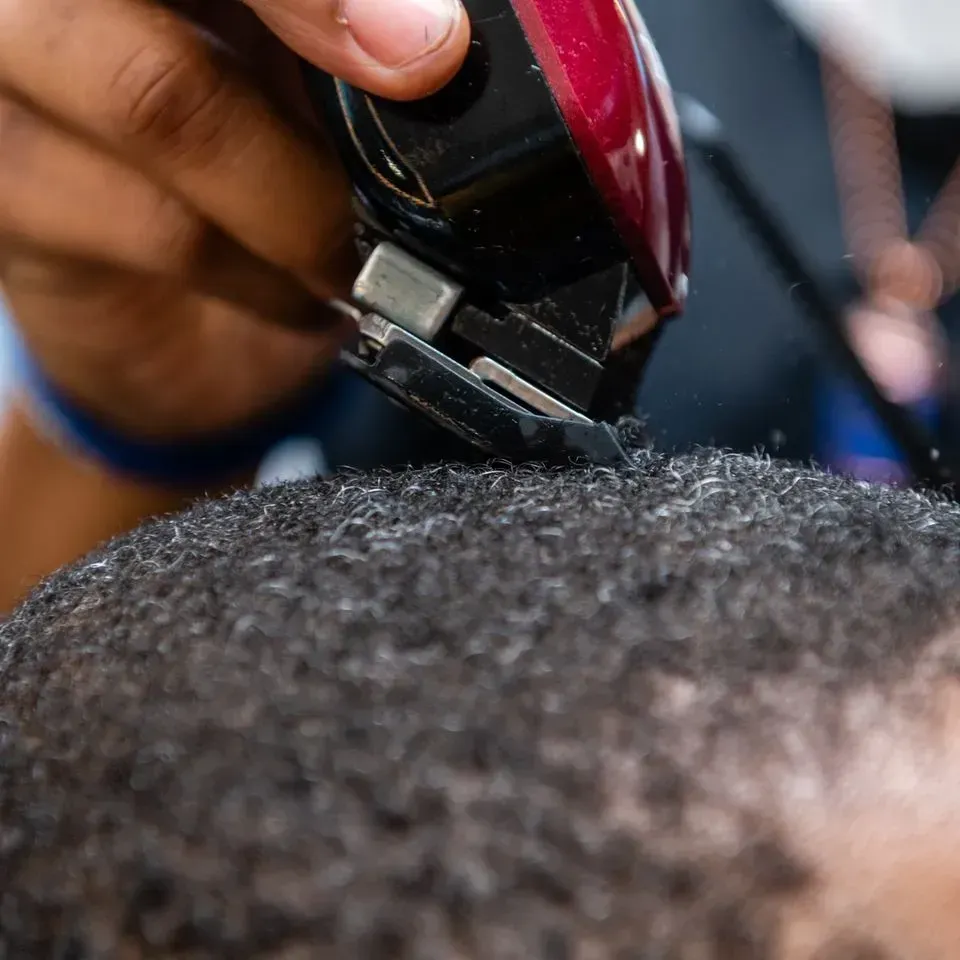 A barber uses electric clippers to trim hair on a person's head.