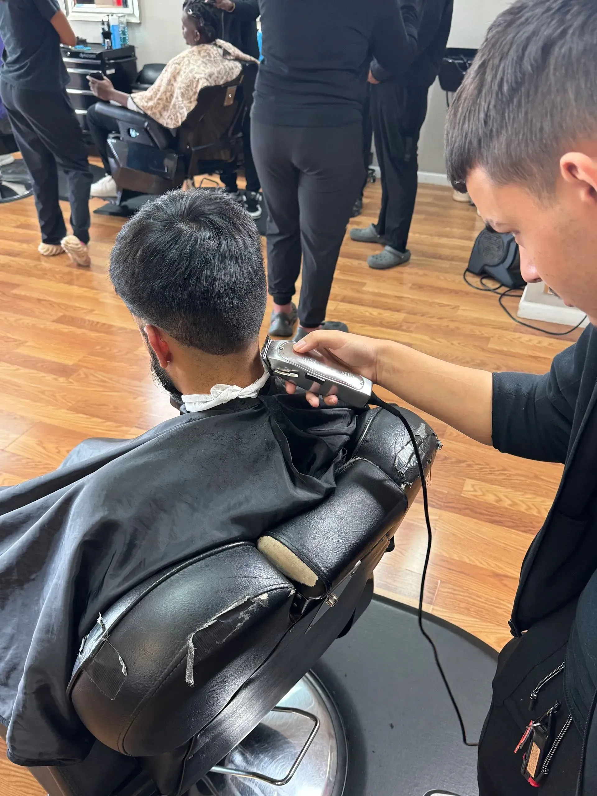 A barber uses clippers to trim the neckline of a client seated in a salon chair.