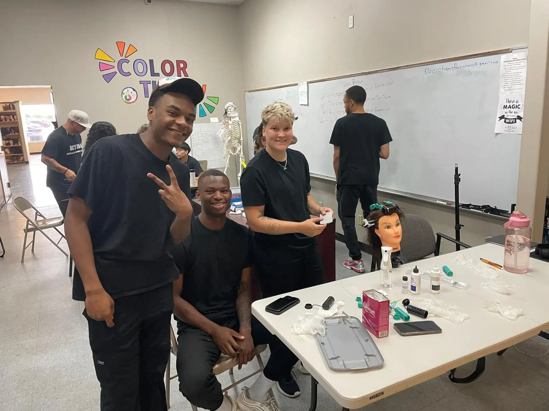 A classroom setting with students around a table, including a mannequin head, with others in the background.