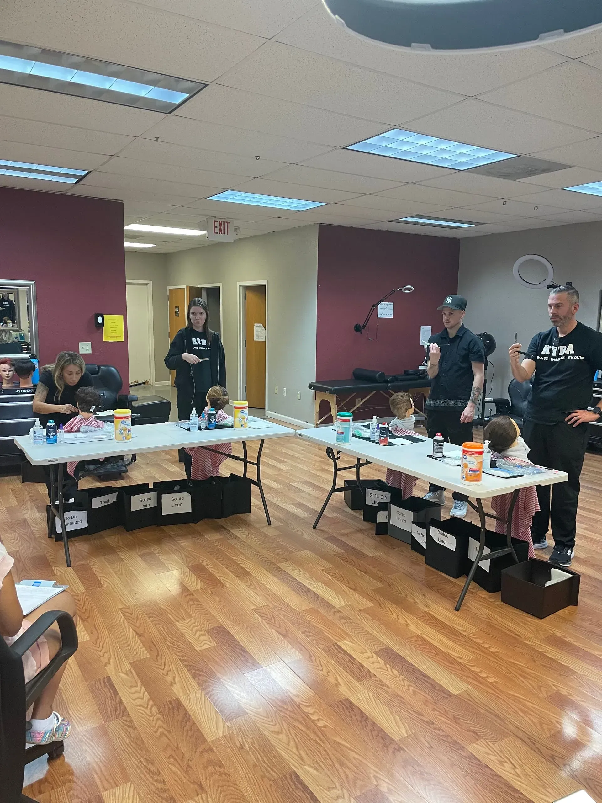 People stand behind two tables in a brightly lit room, organizing materials for a group activity.