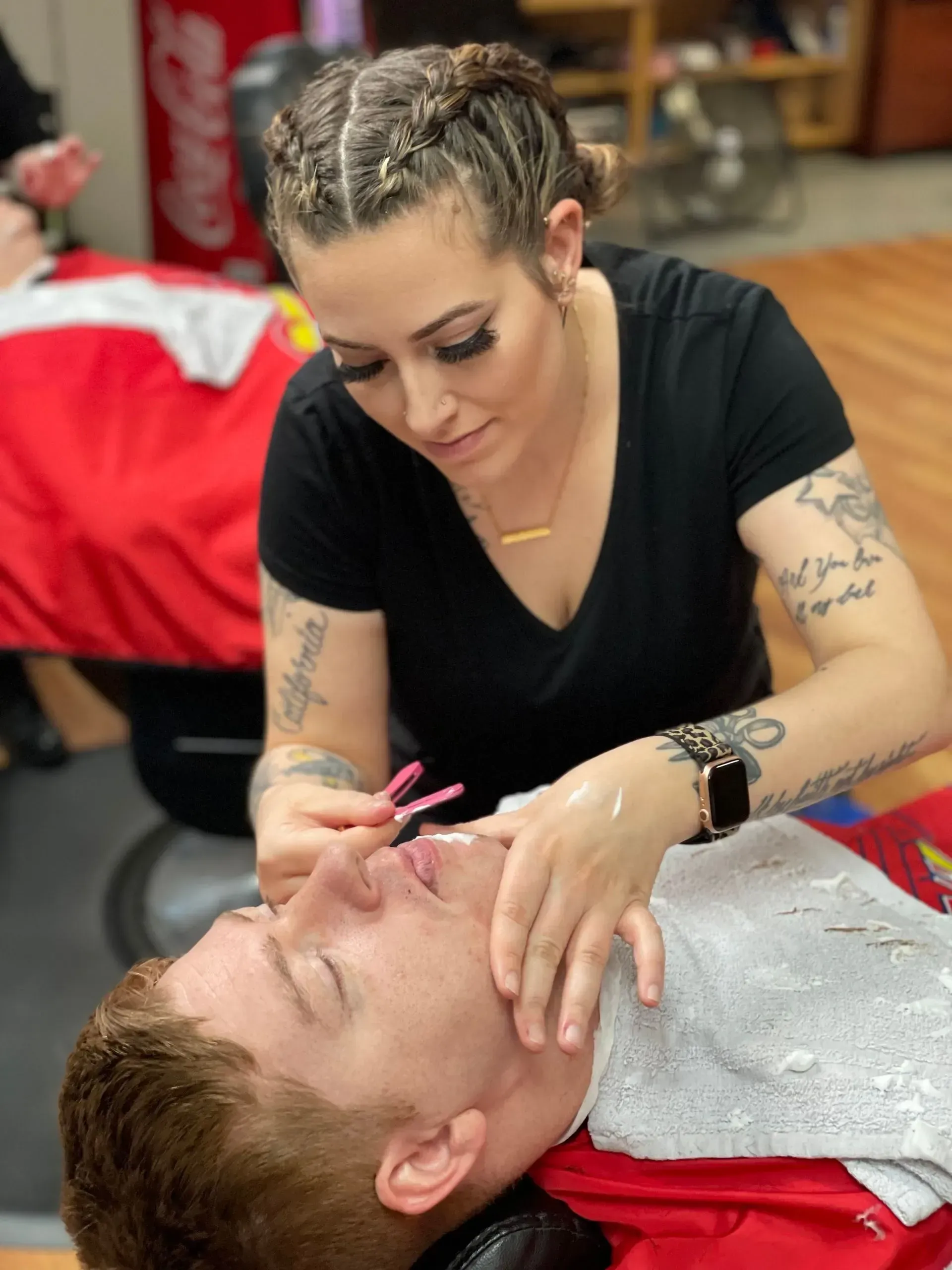 A professional in a black shirt applying cream to a client's face during a grooming service in a barbershop.