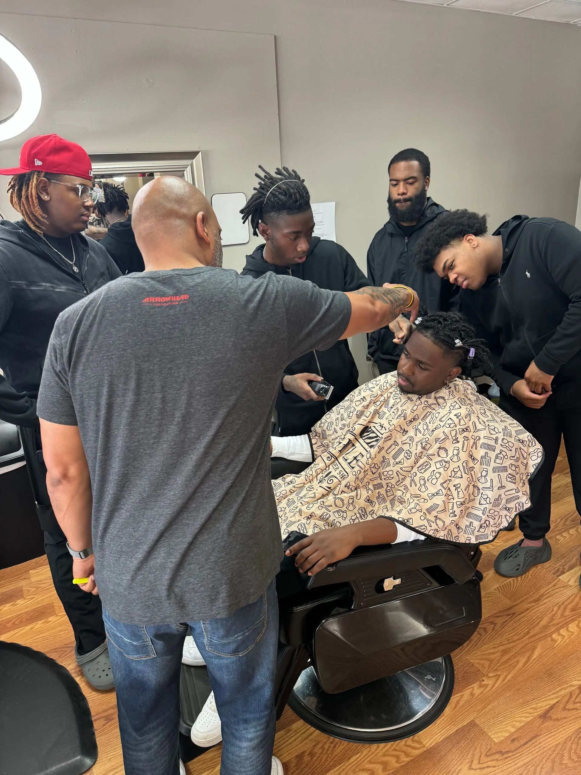 A barber cutting a client's hair in a salon while a group of people watch closely.