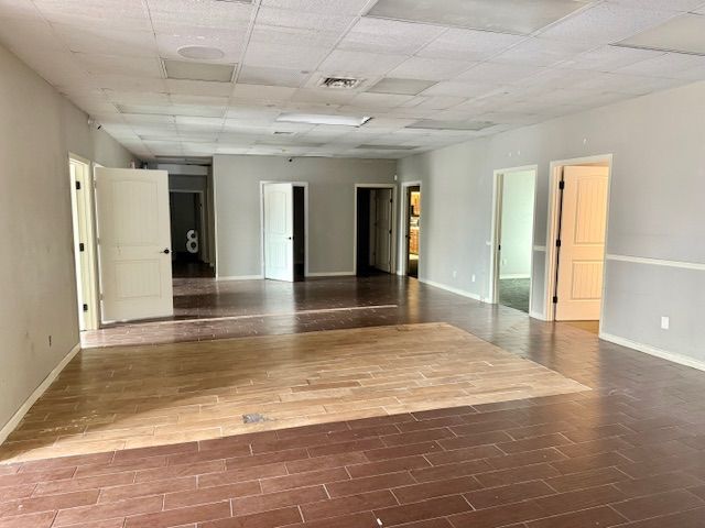 Interior view of an empty room with several open doorways. The room has dark wooden flooring and light gray walls.