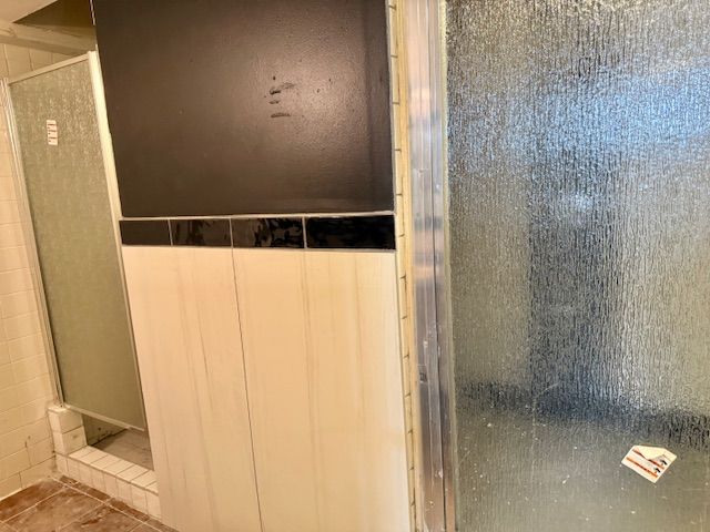 Bathroom interior with a shower and a partial wall. The wall has a dark gray top, a black tile stripe, and white panels below.