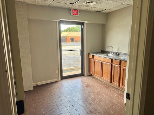 An empty room with a sink and cabinetry. A glass door leads outside to a parking lot.