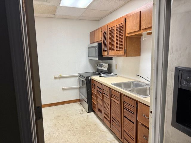 Small kitchen with wood cabinets, stainless steel appliances, and a double sink. Beige tiled floor.