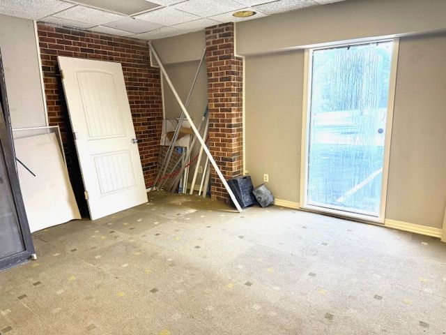 Empty room with a brick wall section, two doors leaning against it, and a glass sliding door. The floor has worn carpet.
