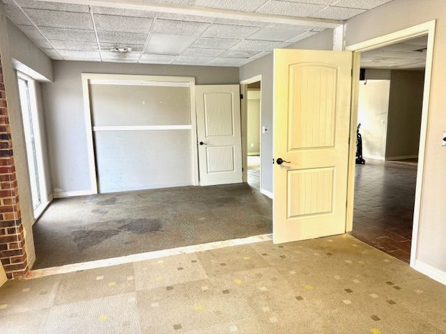 A room with dirty carpet, a brick wall, and several white doors leading to other rooms.