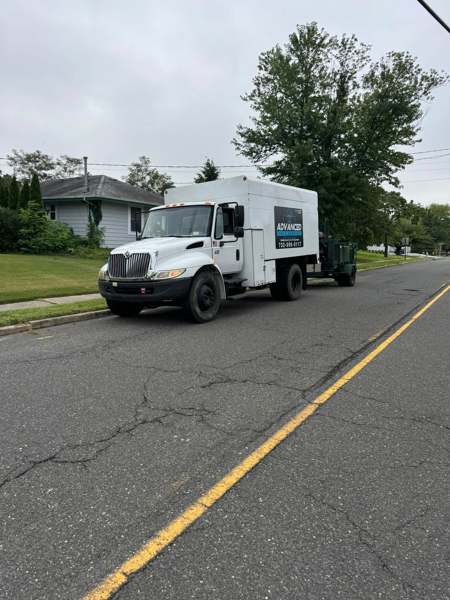 White utility truck parked on a cracked asphalt road next to a grassy curb. A small trailer is attached.