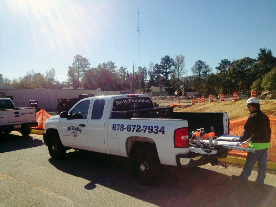 White work truck with phone number, worker carrying equipment in construction zone.